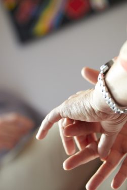 Detailaufnahme einer Handbewegung während eines Gesprächs, im Hintergrund unscharf ein sitzender Mann – symbolisiert konzentrierten Austausch in professionellem Umfeld.
